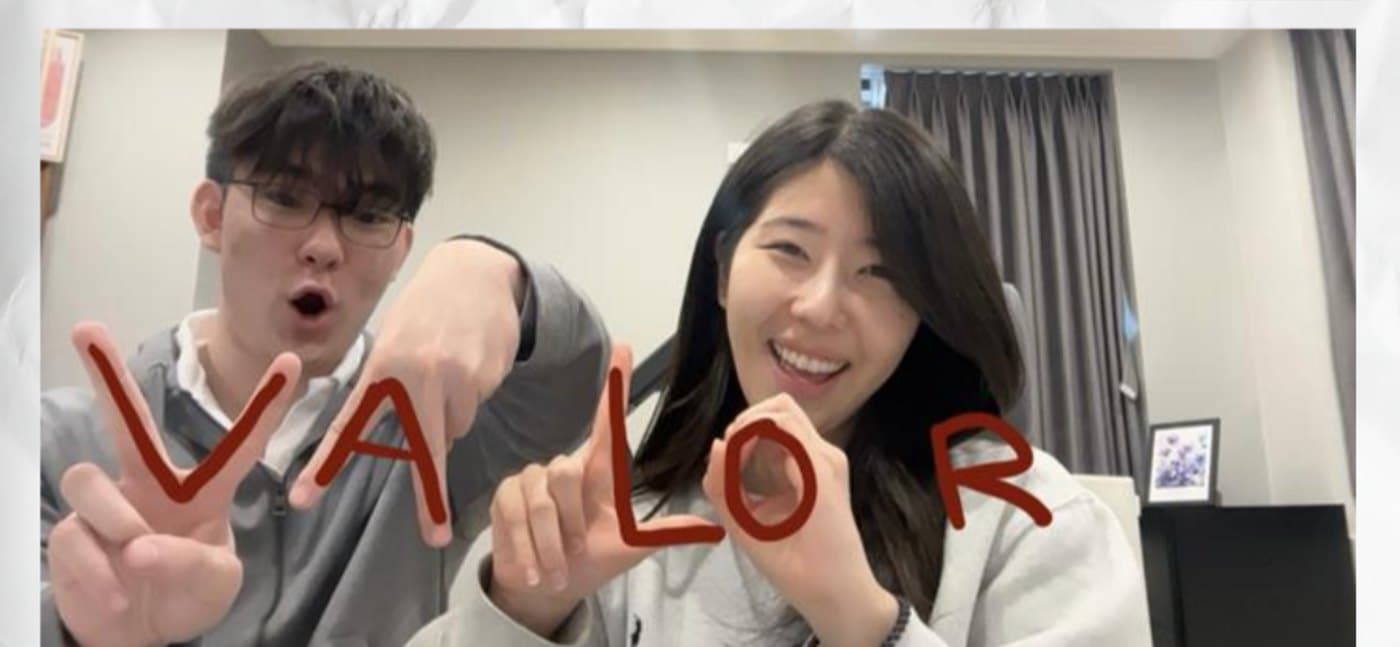Two students spelling VALOR with their hands in front of a dorm window