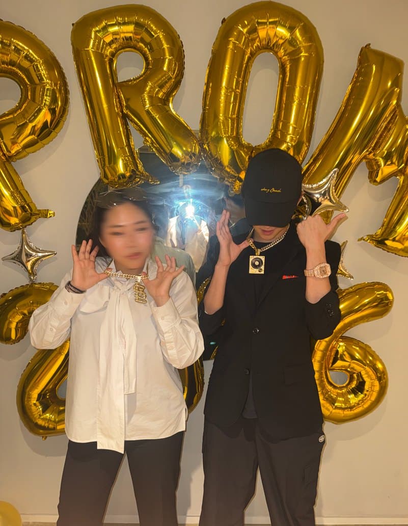 Gold foil balloons spelling PROM, with students posing beneath them