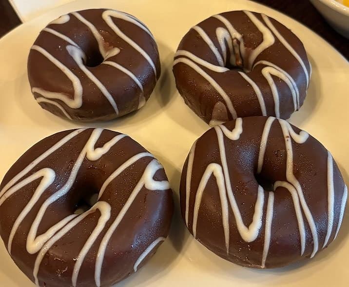 Four chocolate donuts drizzled with white icing on a plate