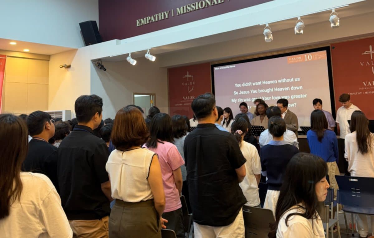 Students and staff standing for worship in the chapel, lyrics projected on the screen behind the band