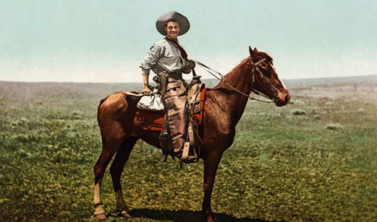 A hand-tinted photograph of a cowboy on a chestnut horse on open prairie