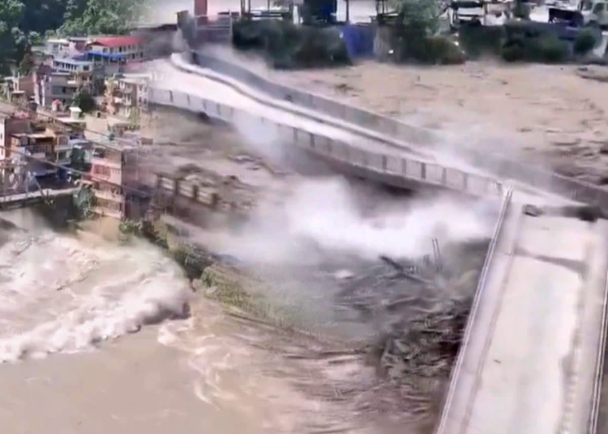 Brown floodwater tearing through a bridge between river towns in Nepal
